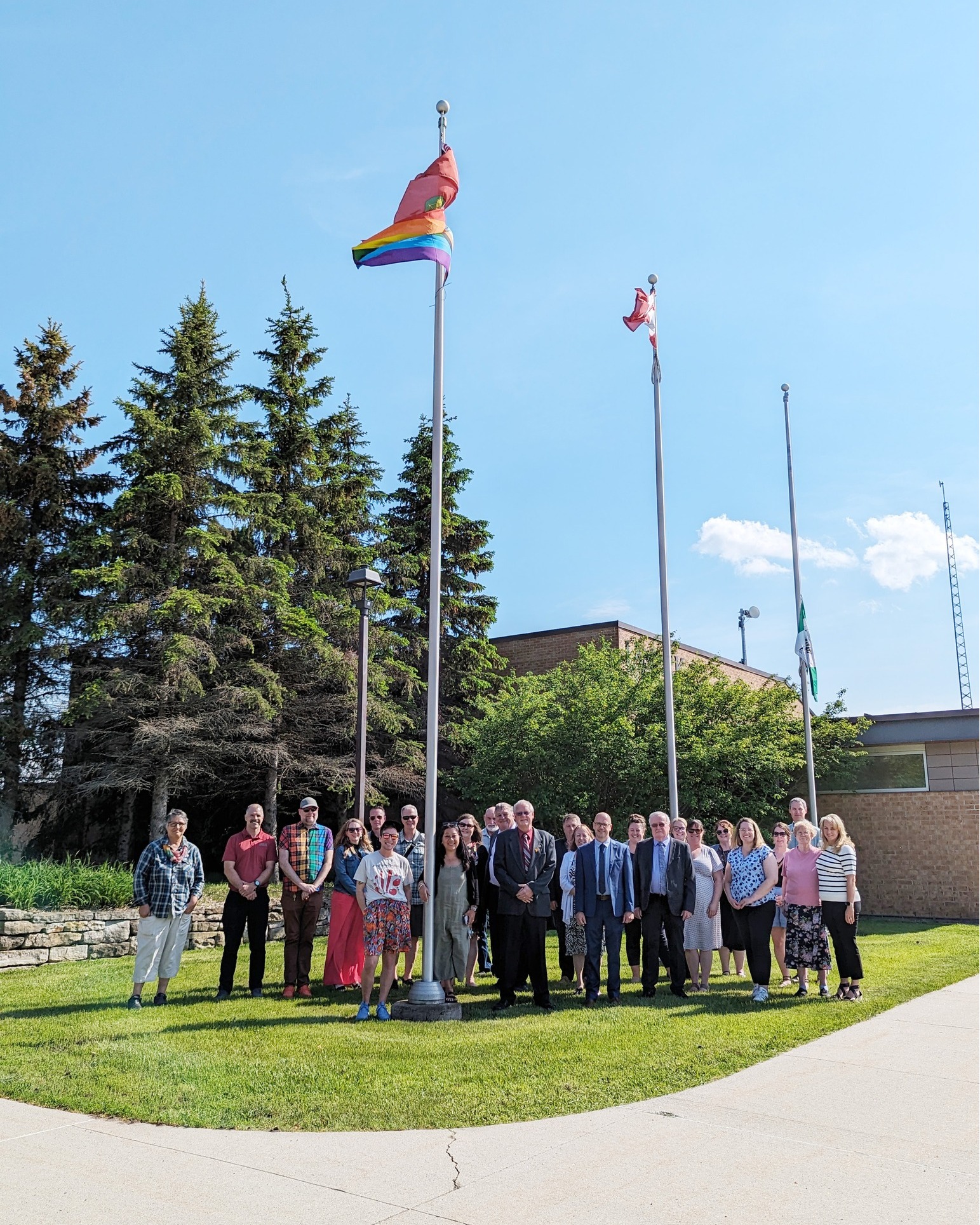 Group of people stand outside of a brick building in front of three flag poles