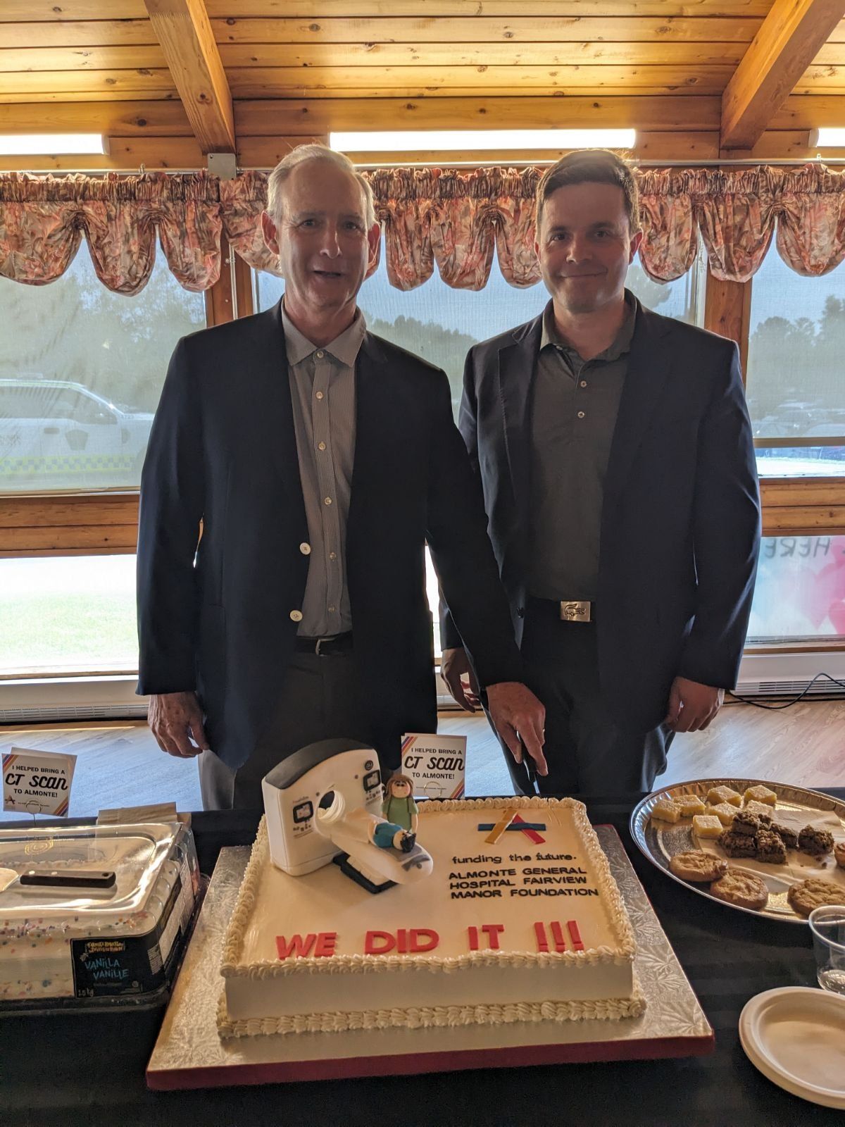 Two men stand behind a cake, ready to cut it