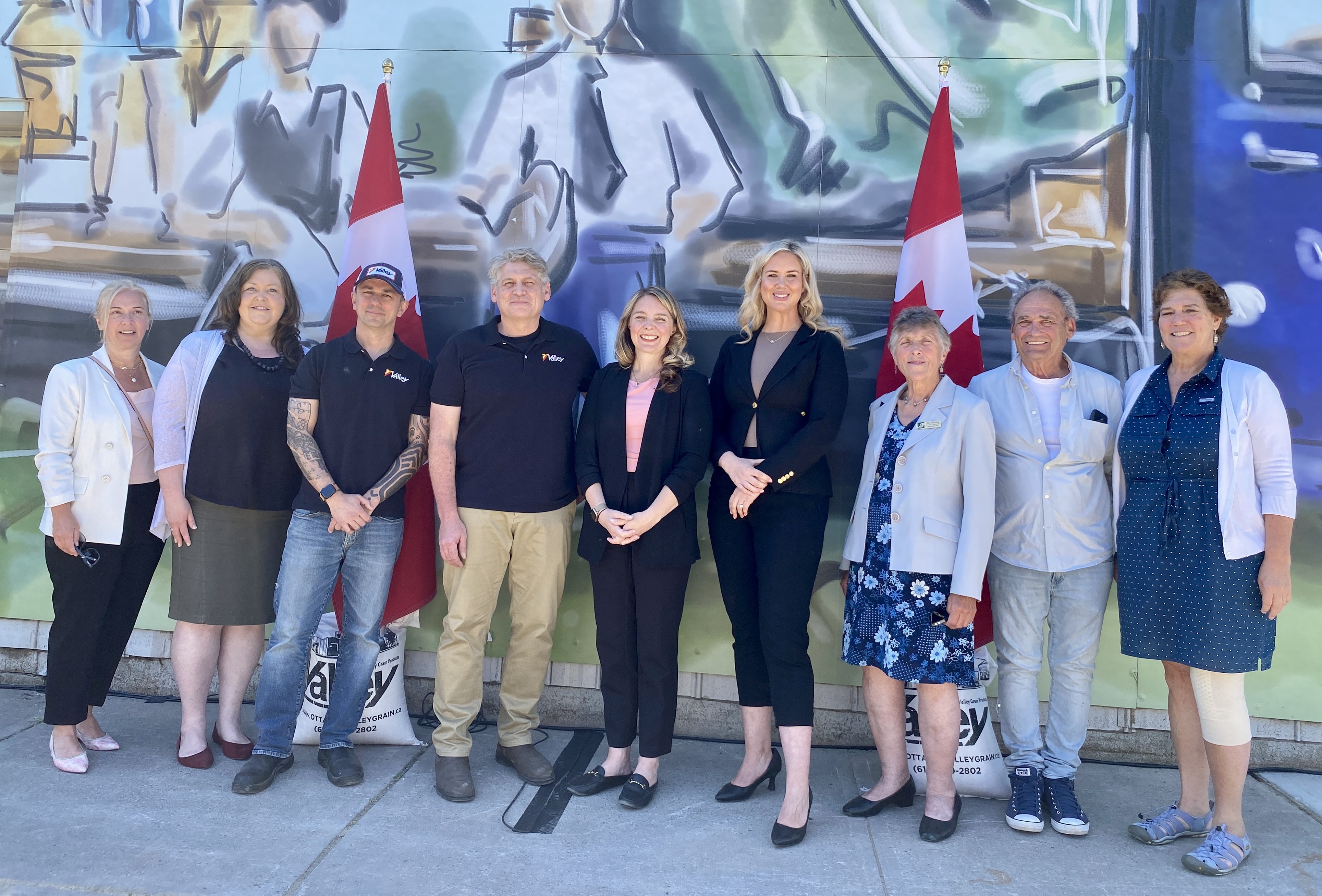 Group of people stand outside against a backdrop of a mural on a building