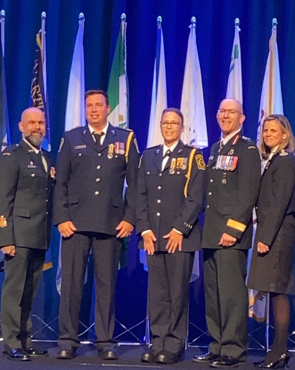 Photo of paramedics in formal uniforms lined up in front of flags after receiving medals