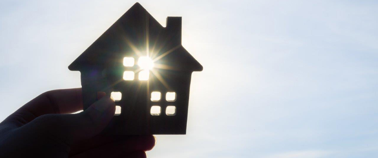 A figurine of a house is held up to the sun