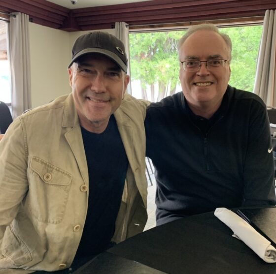 Two men seated at a table smile at the camera