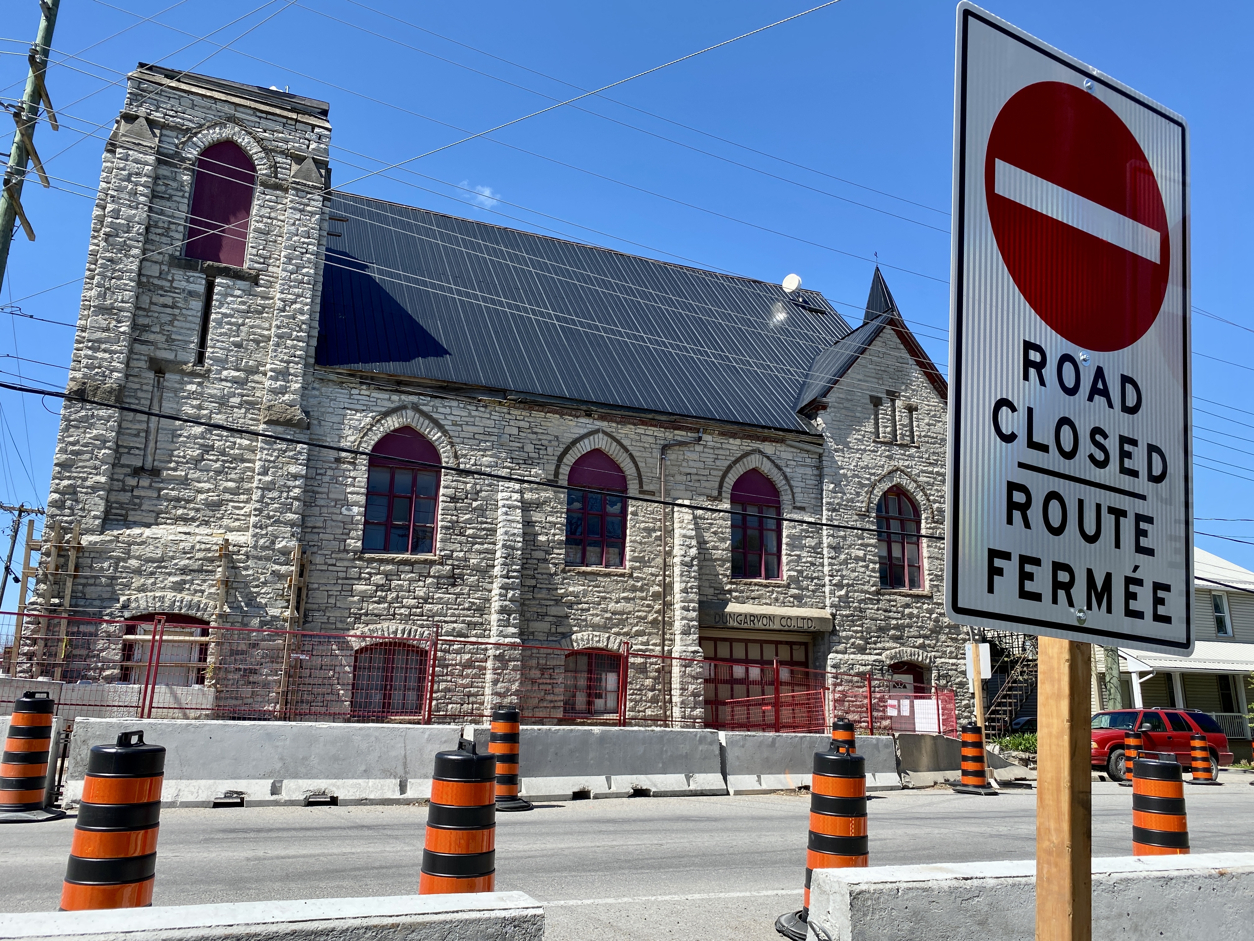 Photo of a multi-storey stone building with concrete barriers and pylons in the foreground. A large 'Road Closed' sign can be seen to the right.