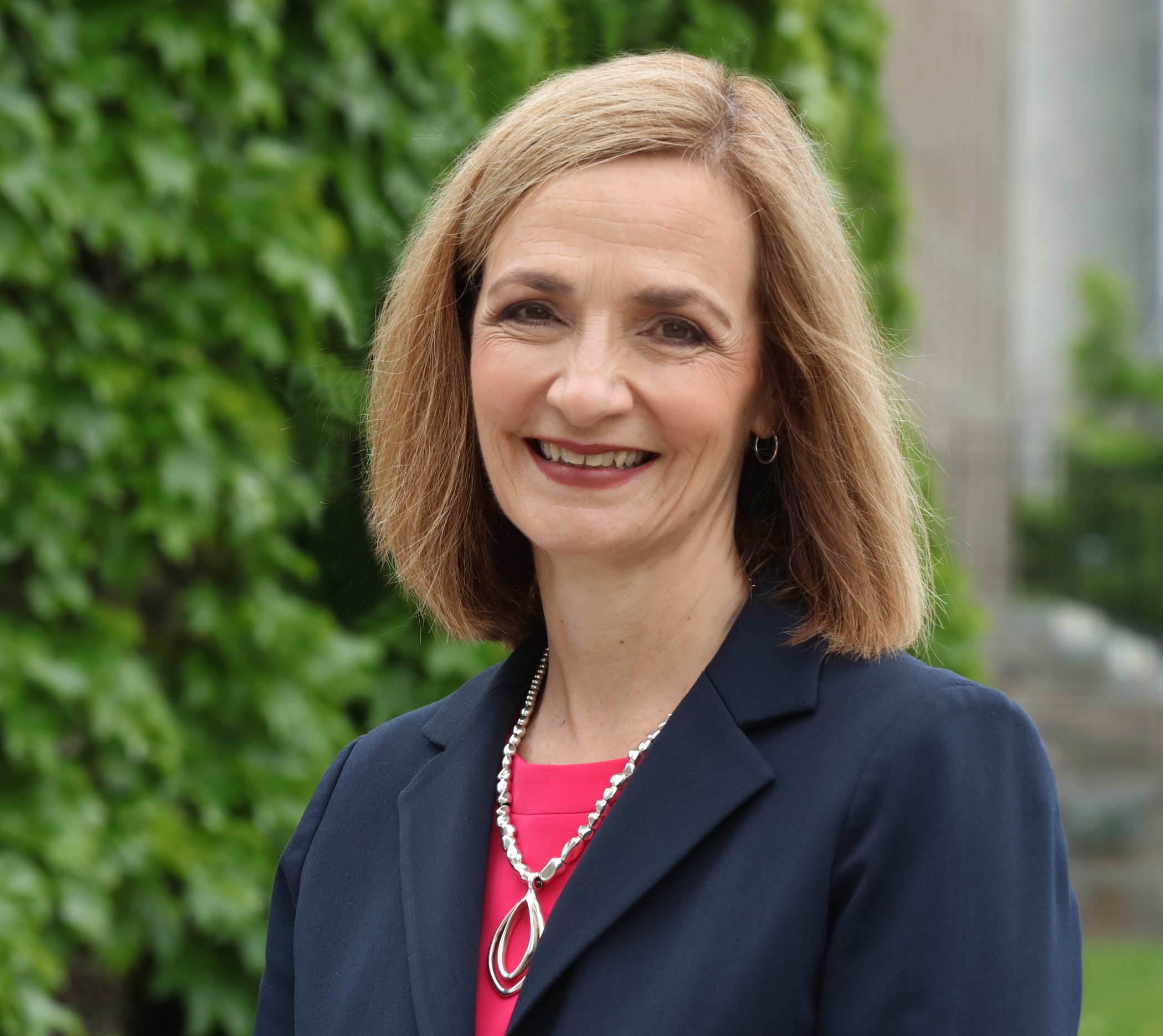 Woman in blue blazer stands in front of a garden