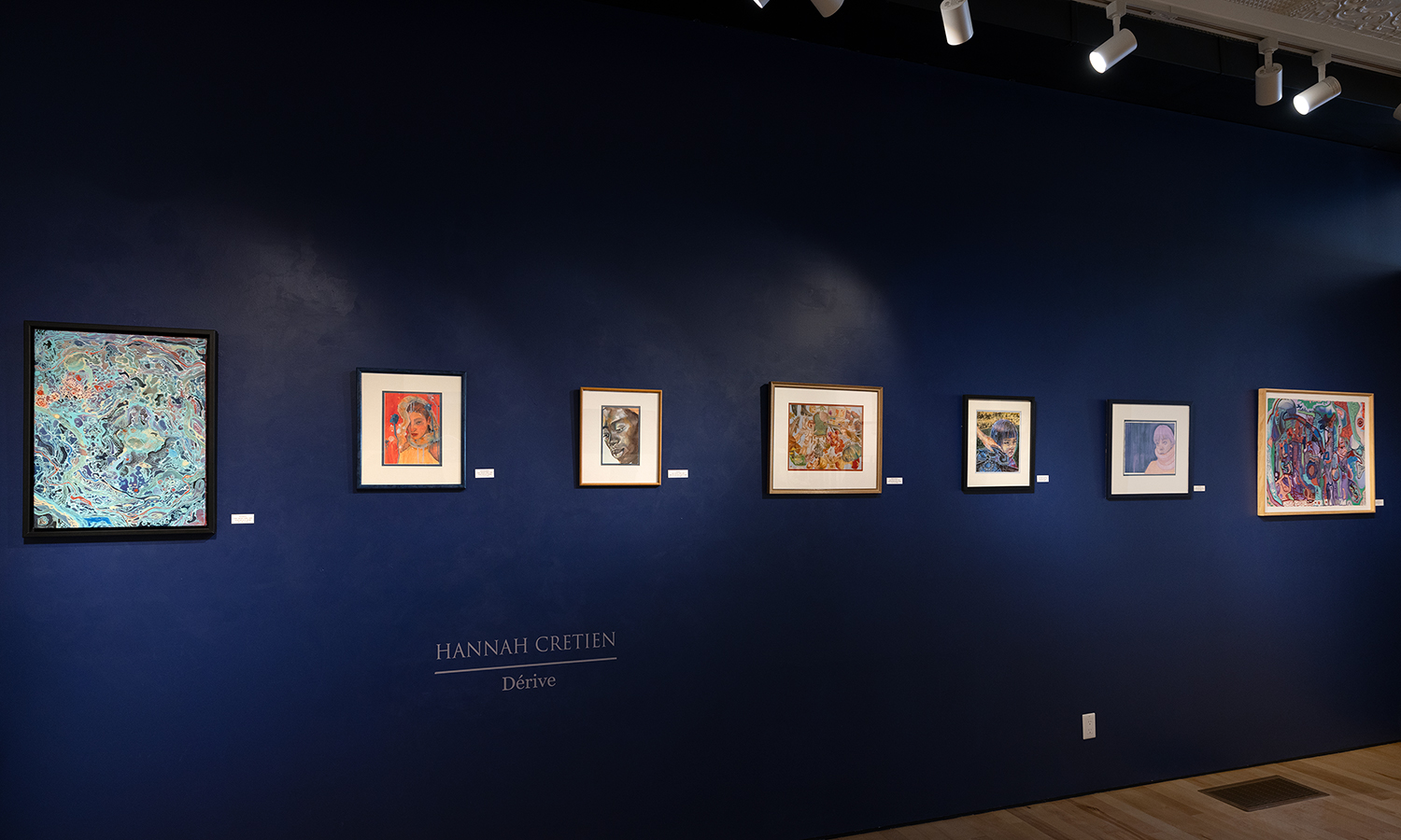 Colourful framed artwork arranged on a navy blue gallery wall