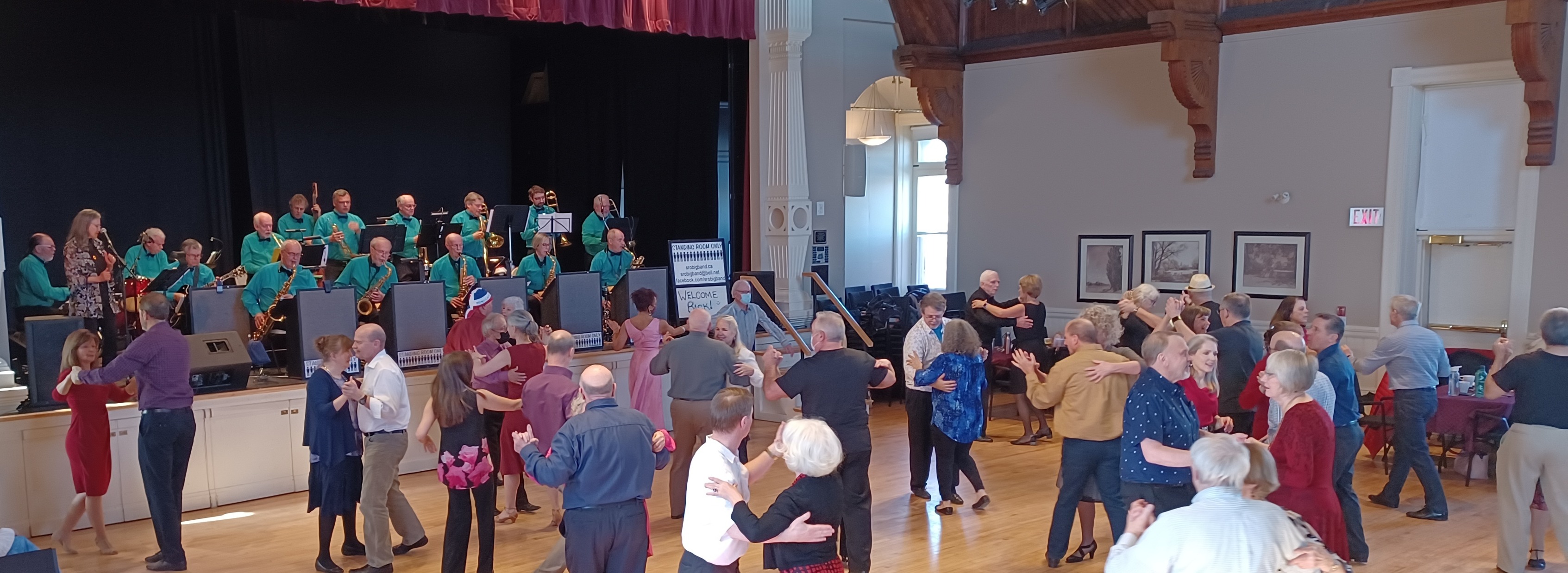 Couples dance in an auditorium while a band plays on stage