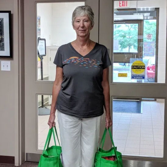 Woman stands in front of a glass door holding two green cloth bags