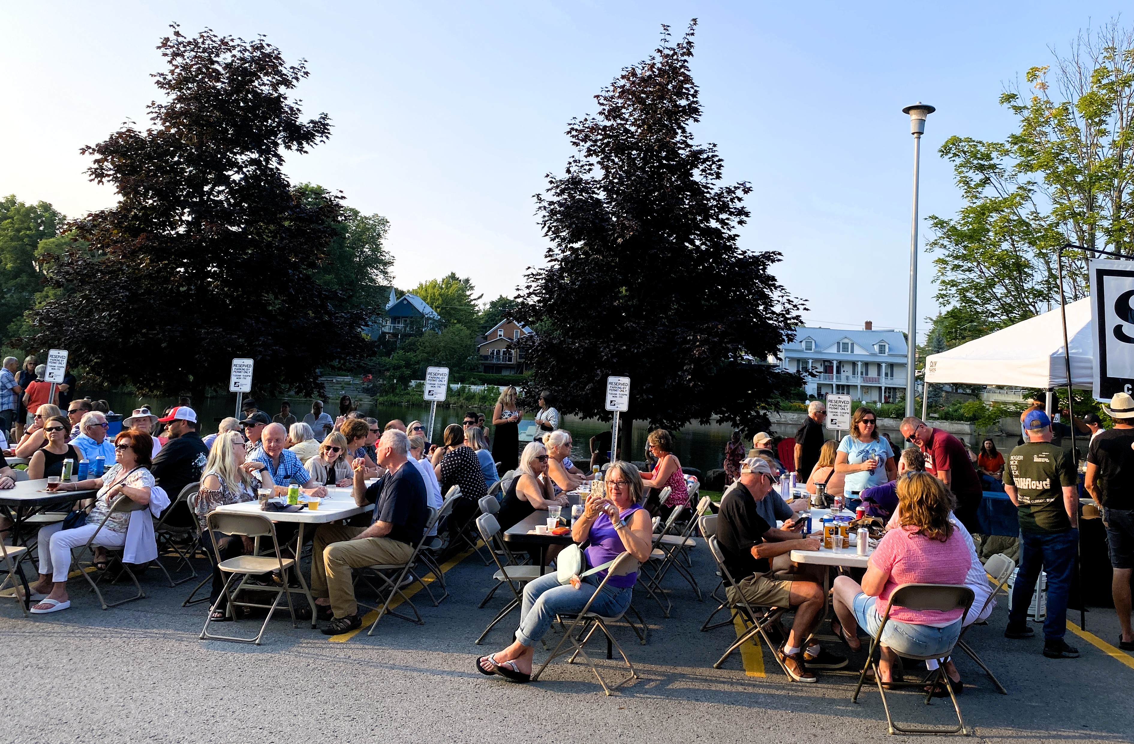 Groups of people sit at tables outside in a parking area