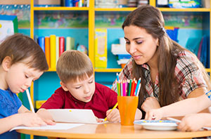 Photo of a daycare teacher with two children at a desk