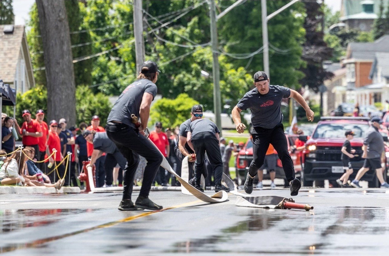 One man holds a fire hose while another tries to pick up the other end during a skills competition
