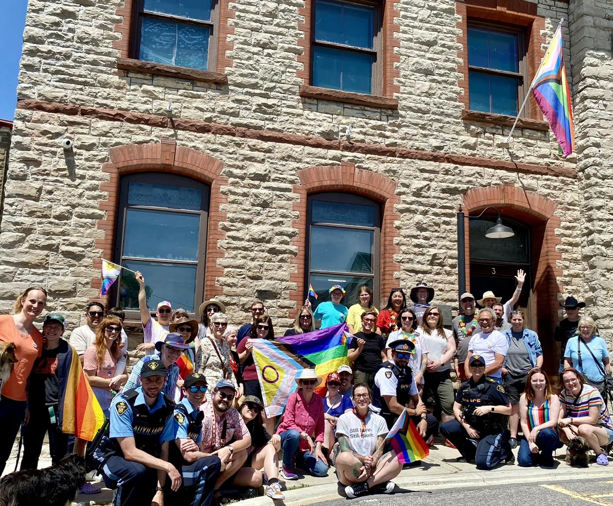 Group of people stand in front of a stone building with Pride flags