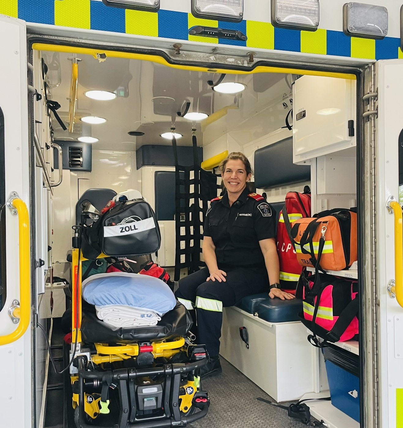 A female paramedic sits inside the back of an ambulance surrounded by a stretcher and medical equipment