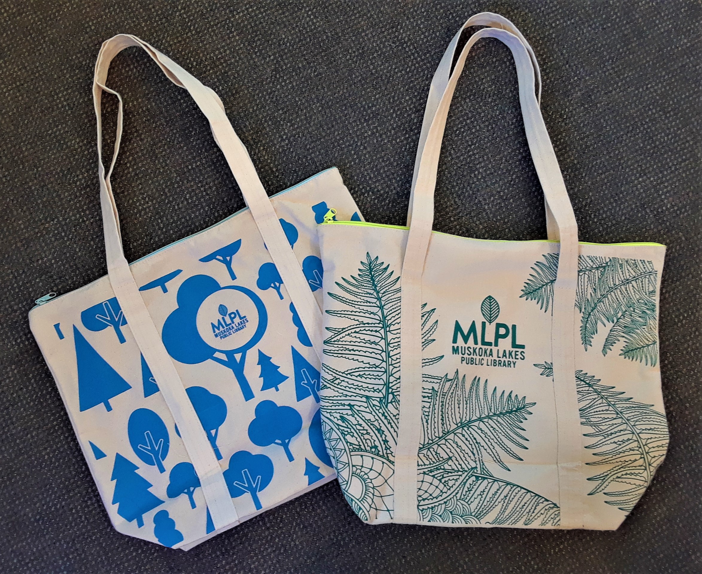 Two canvas tote bags, one with blue graphic trees, one with green fern motif.  Both with MLPL logot.