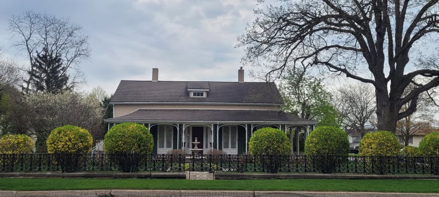 Outside exterior of a designated heritage home in Niagara Falls, showing decorative iron fencing, water fountain and green landscaping.