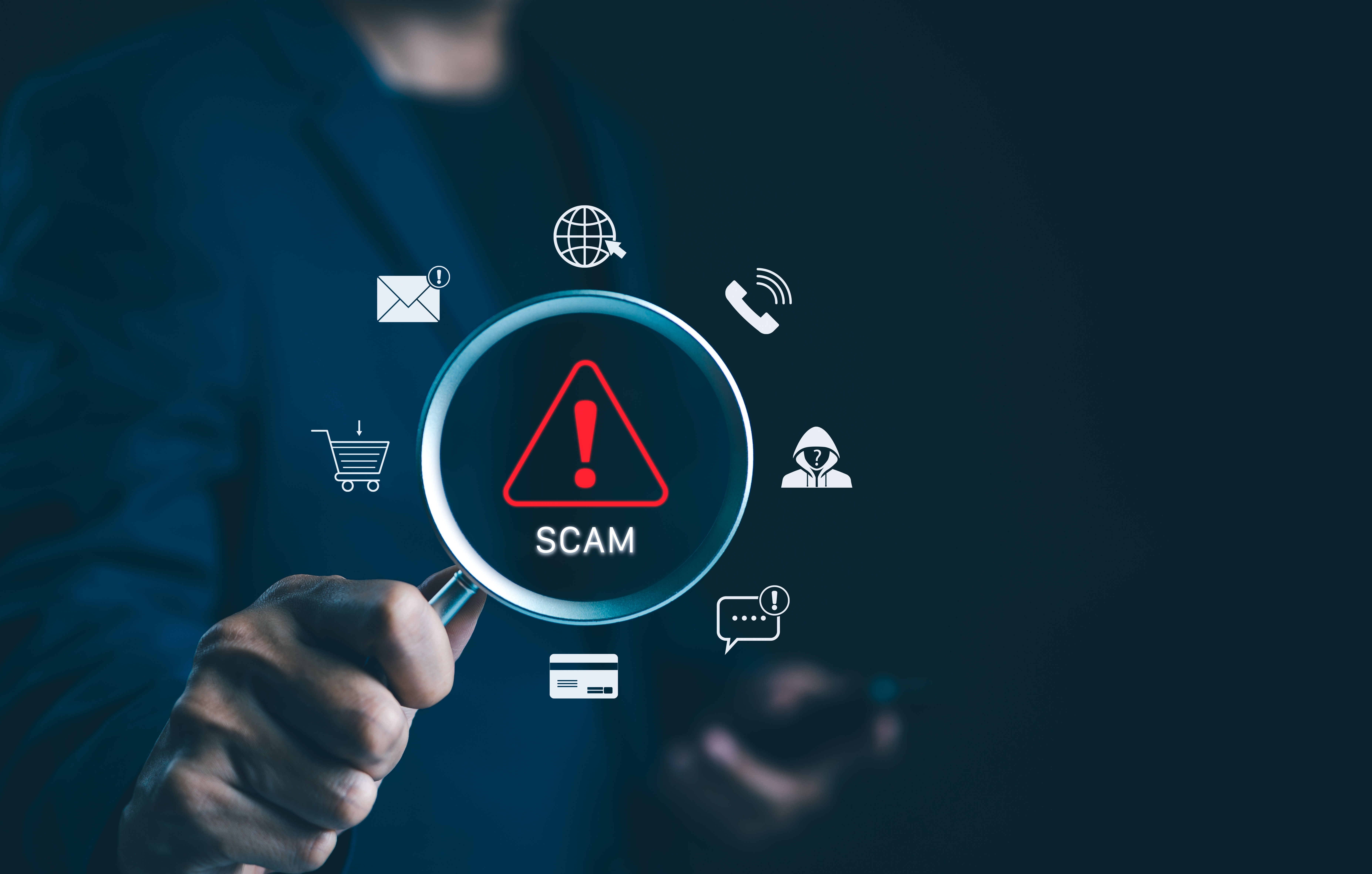 a stock image of a hand holding a magnifying glass with icons for types of scams