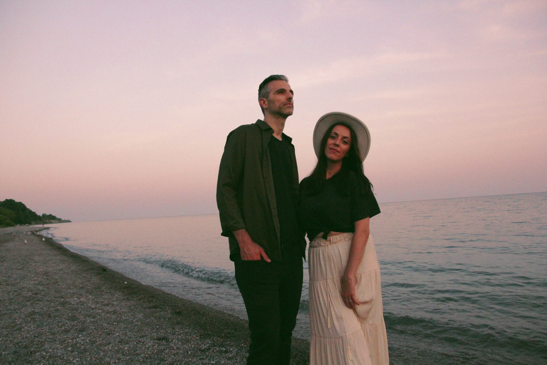 husband and wife standing on beach with sunset