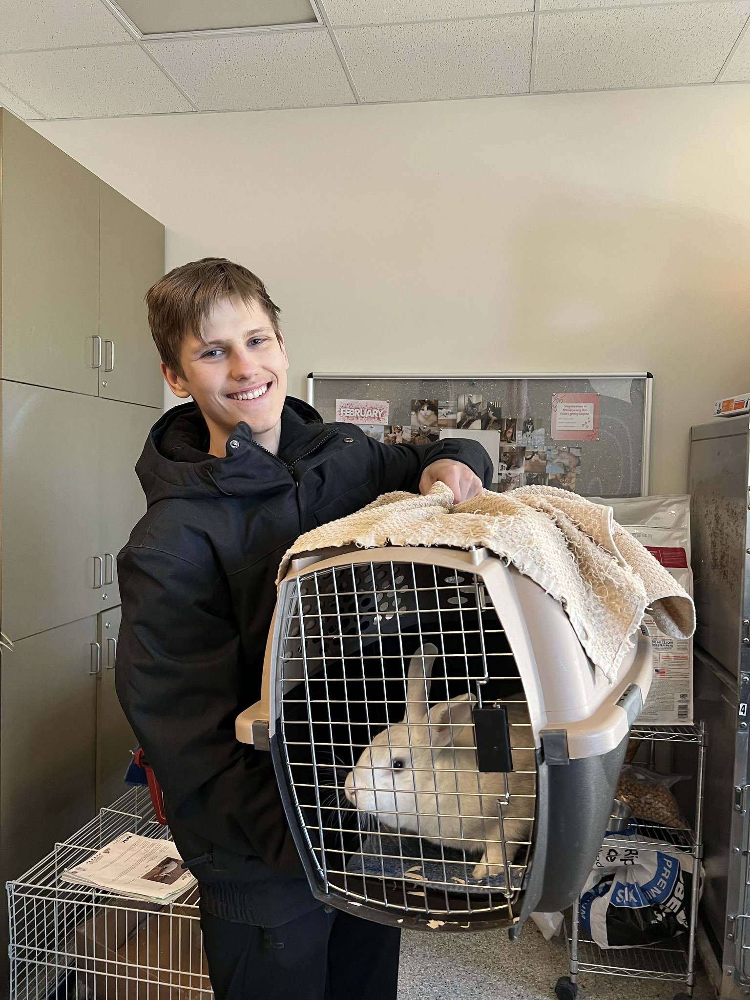 Teenage boy holds a crate with a rabbit. 