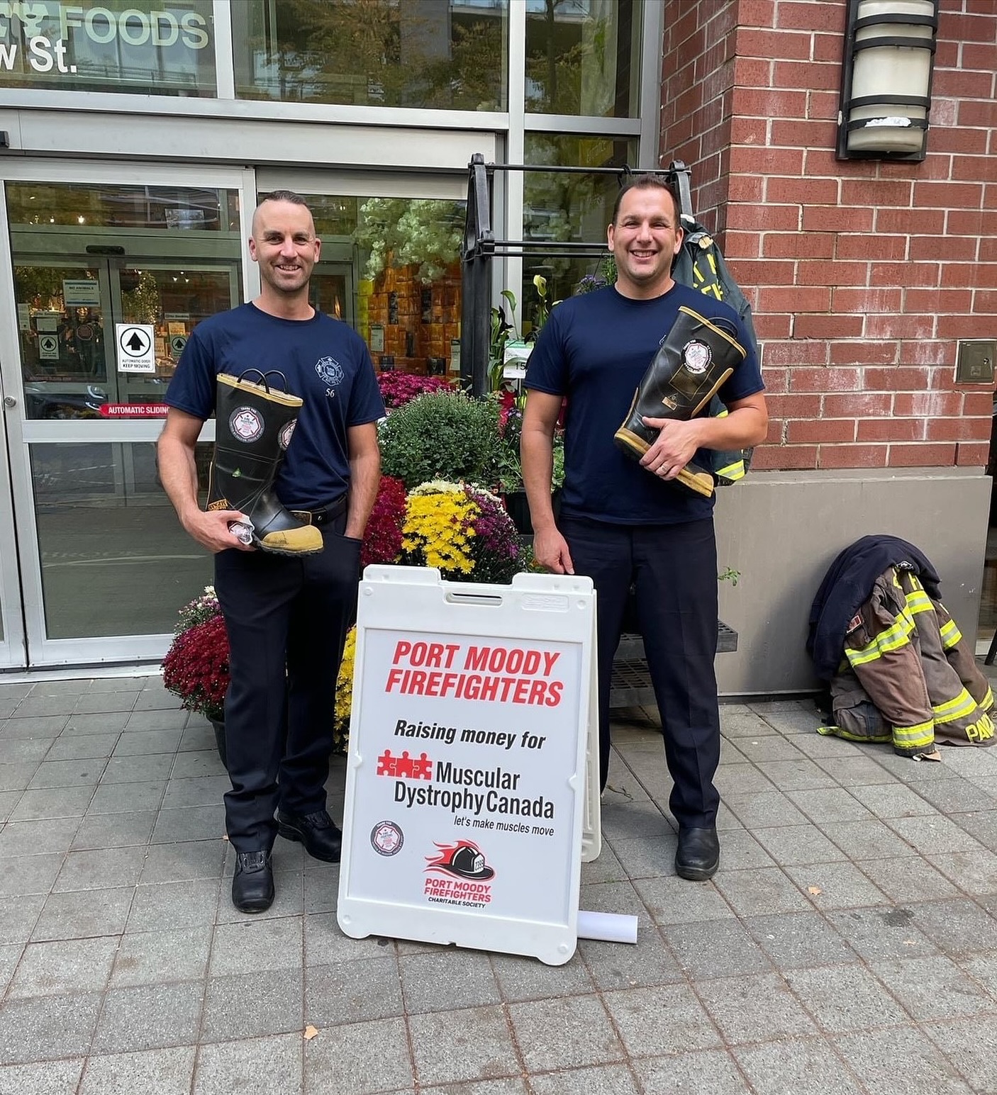 Two off duty firefighters holding a boot in front of a sign