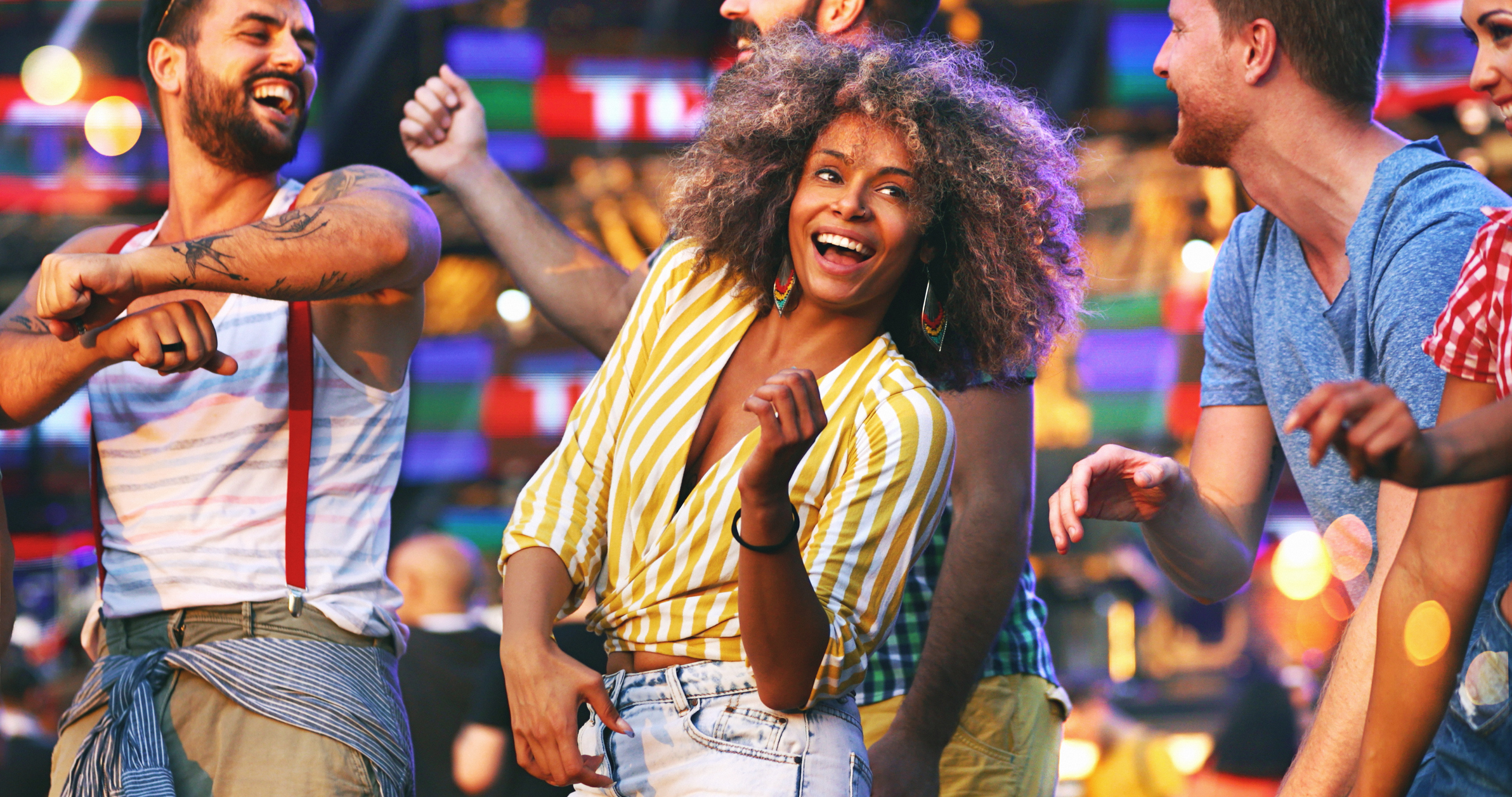 A group of people joyfully dancing outdoors at a festival, surrounded by colourful lights.