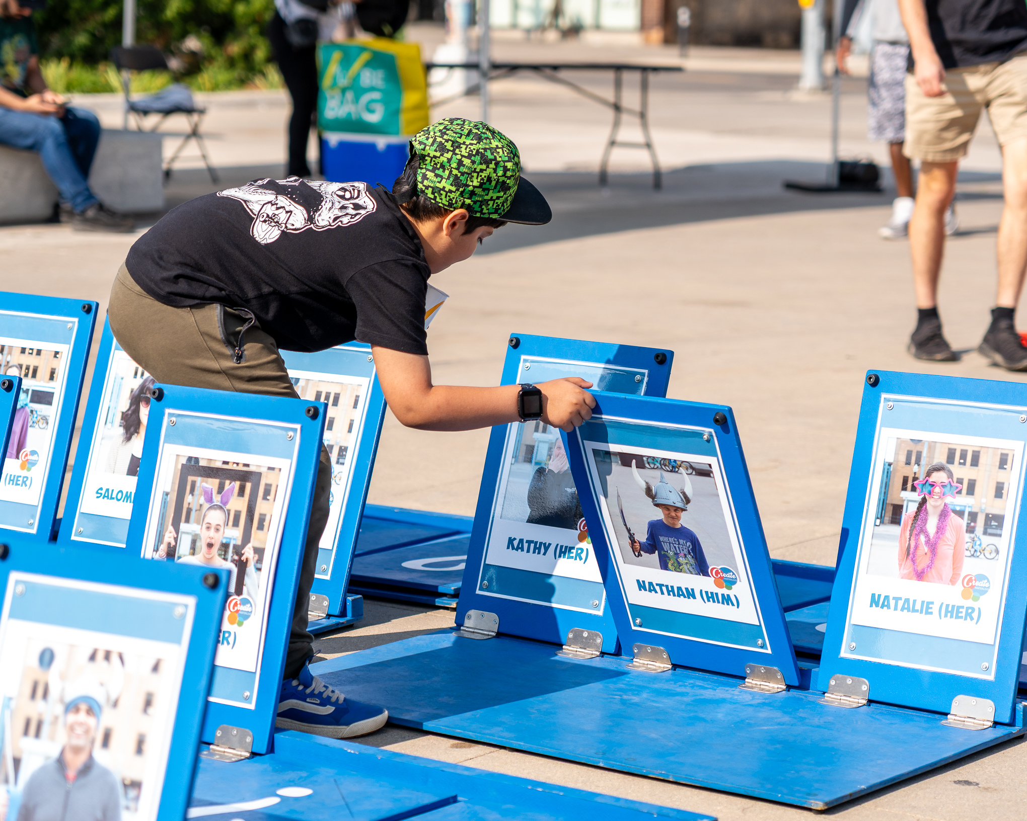 Child play with giant  blue game of 'Guess Who' in outdoor urban area.