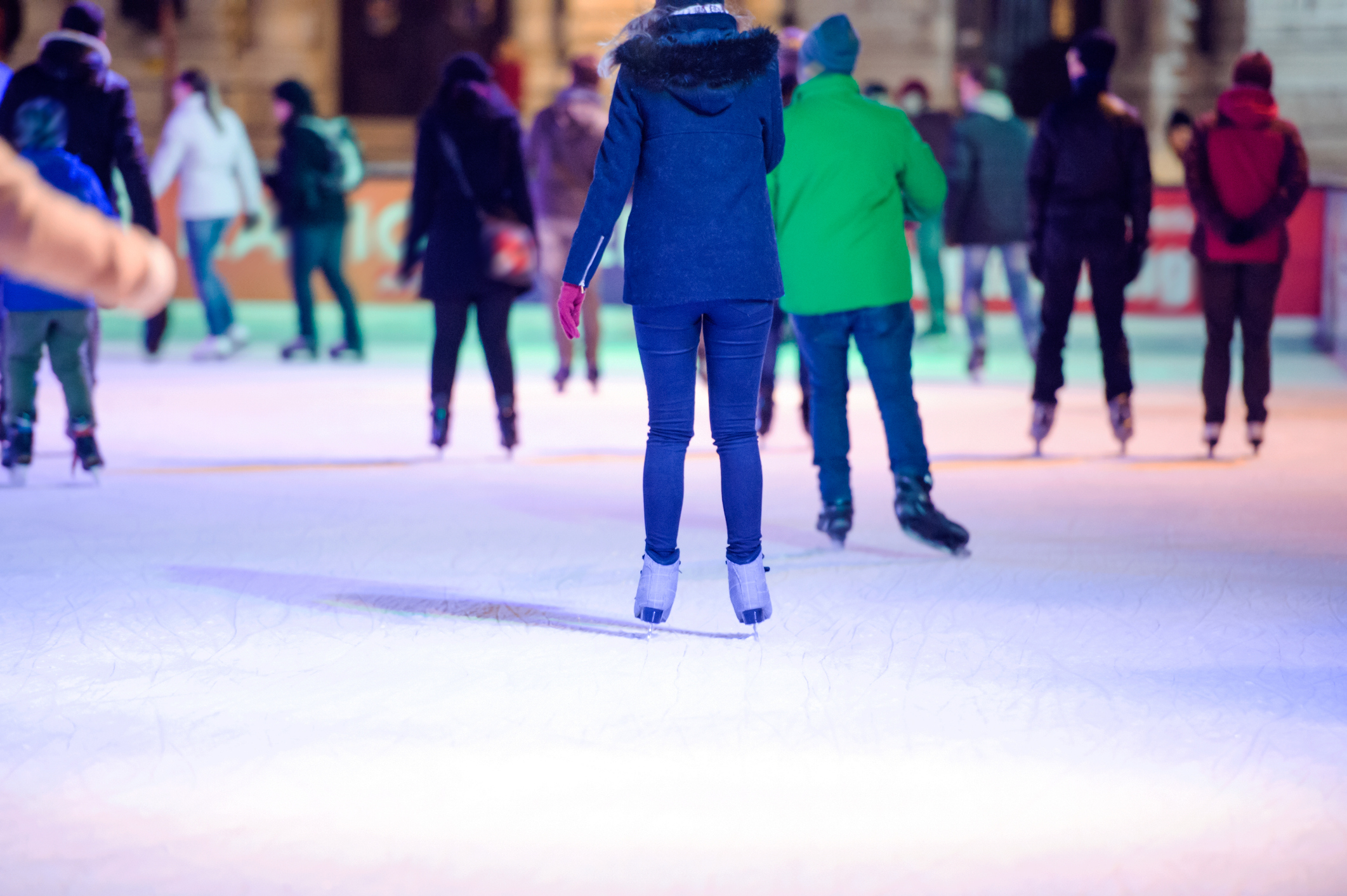 A group of people wearing winter clothes are ice skating on an outdoor rink.