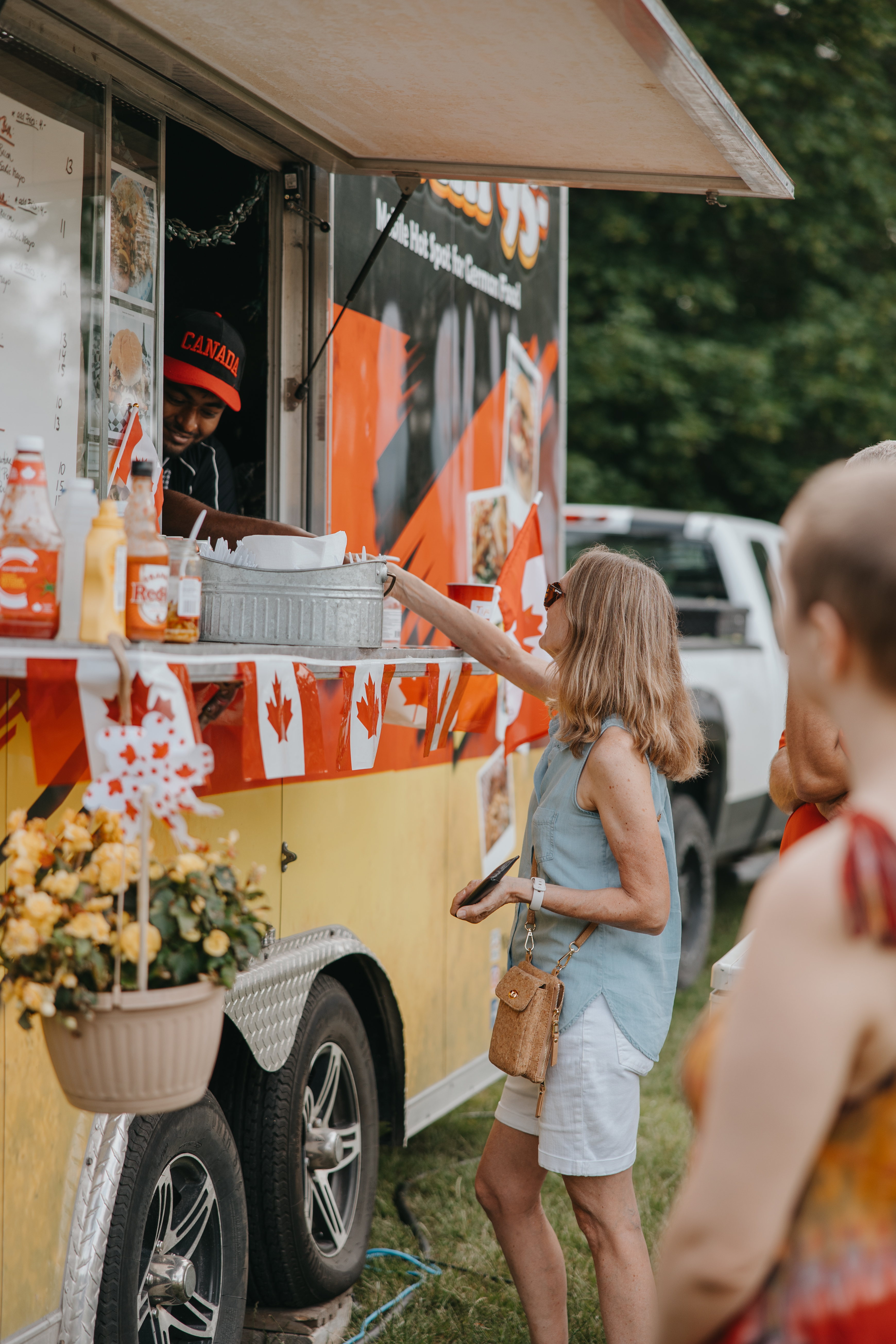 Person stands at food truck window that is decorated with the Canadian flag.