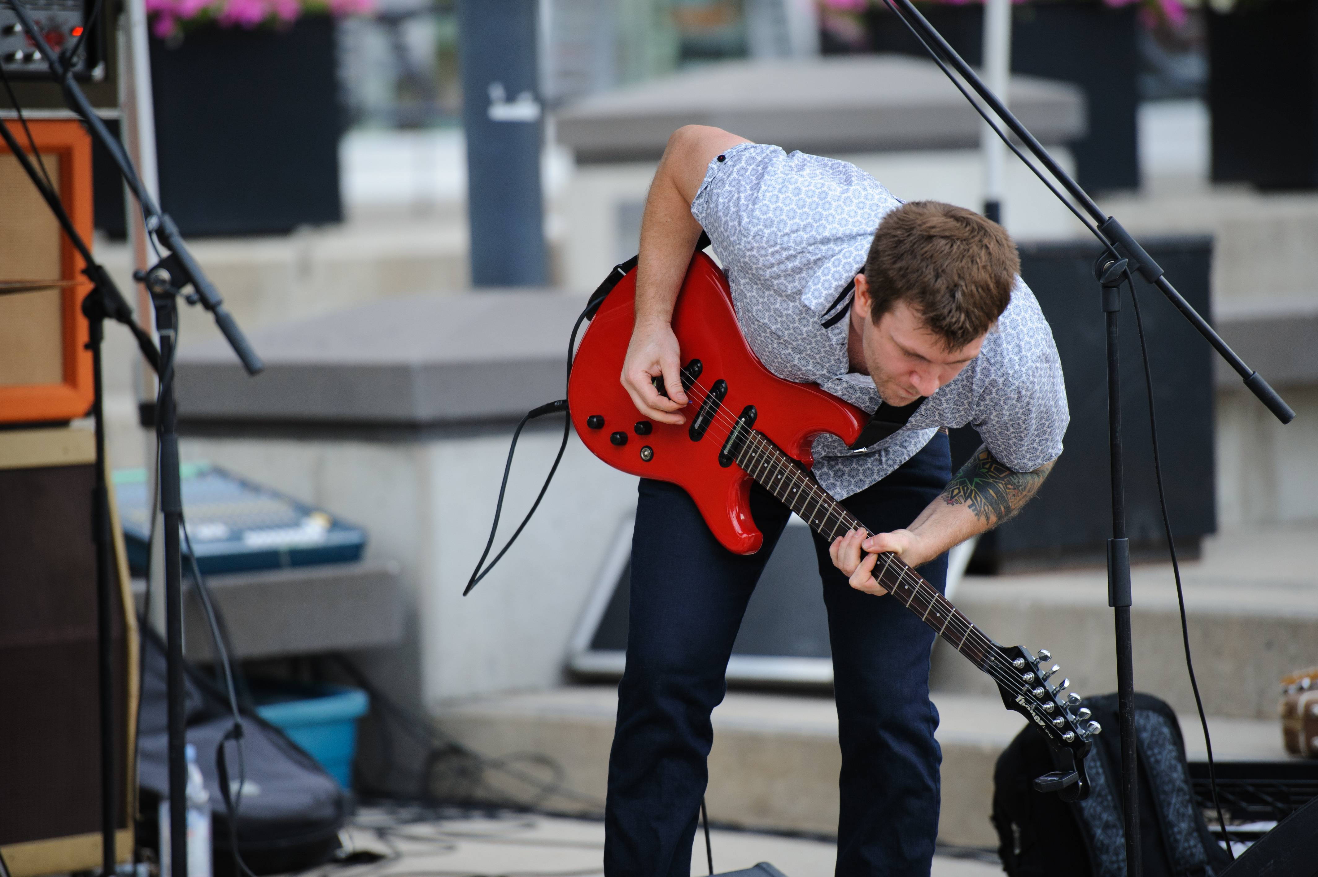 Person stands outdoors in urban area playing a bright red electric guitar.