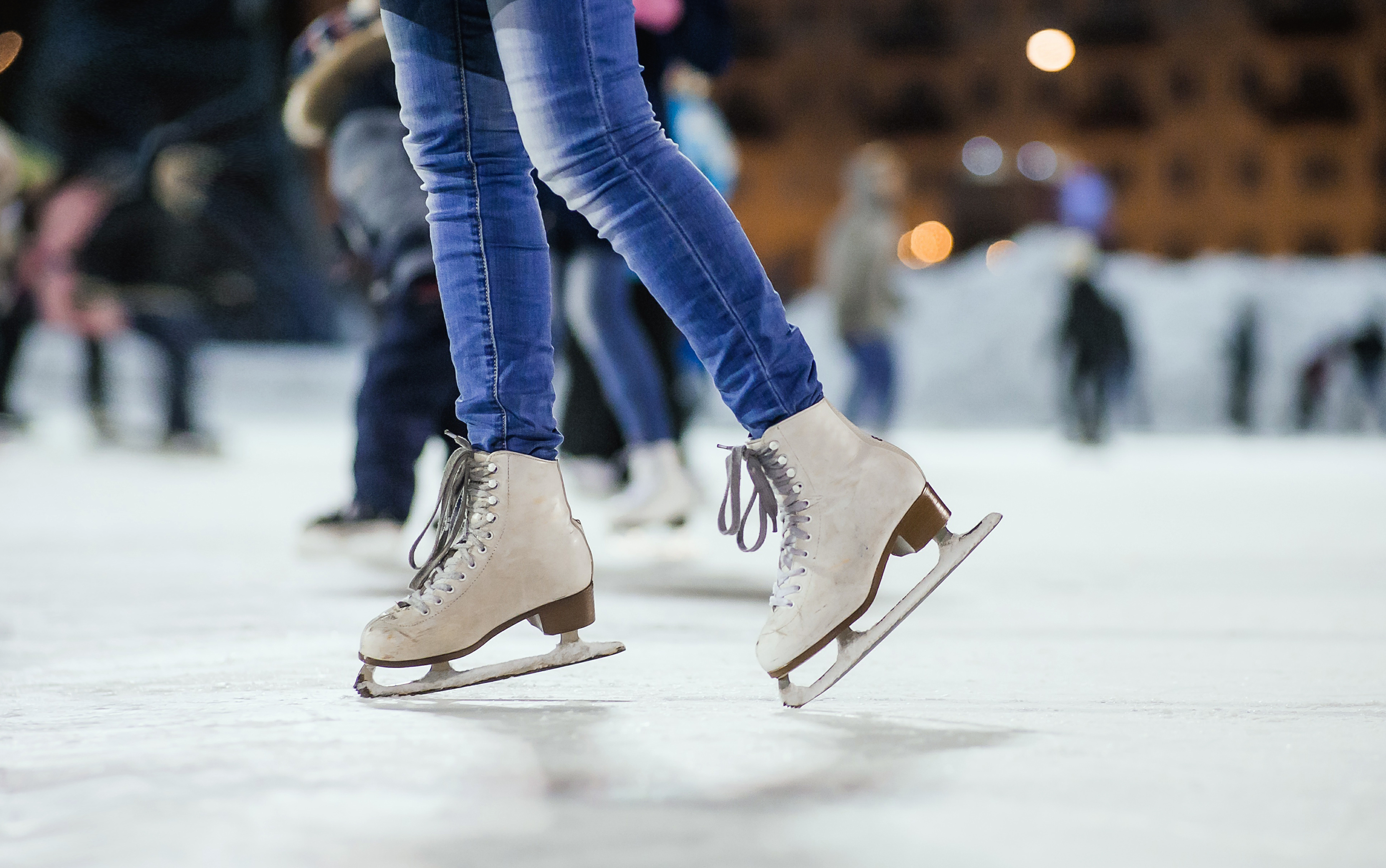 Person figure skating on outdoor ice rink with others ice skating behind them.